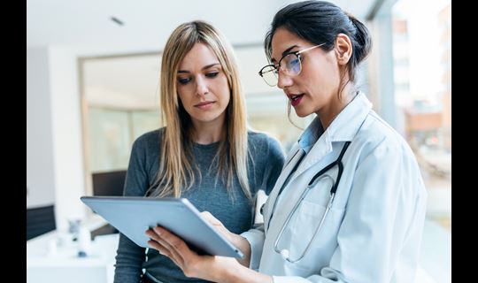 Shot of beautiful female doctor talking while explaining medical treatment with digital tablet to patient in the consultation.