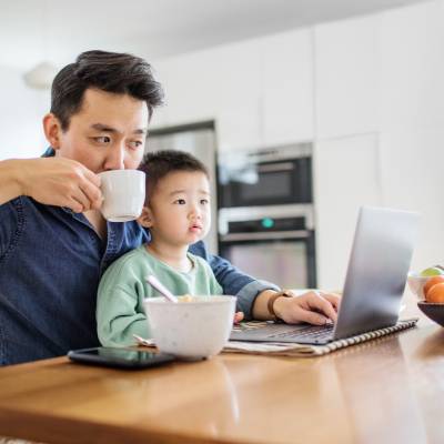 Father multi-tasking with young son at kitchen table
