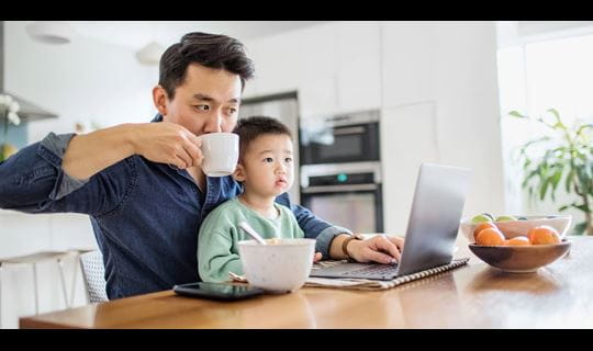 Father multi-tasking with young son at kitchen table
