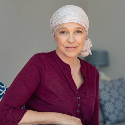 Mature woman with cancer in pink headscarf smiling sitting on couch at home. Smiling woman suffering from cancer sitting after taking chemotherapy sessions. 